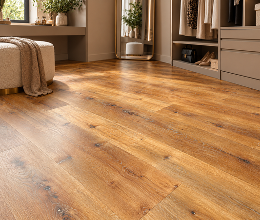Warm medium-brown wood plank flooring shown in a styled room with a bench, draped throw, mirror, and closet area.
