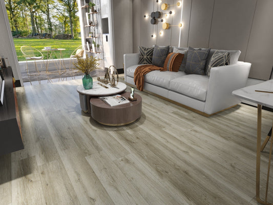 Light oak wood plank flooring shown in a modern, stylishly decorated living room with a white sofa, round coffee tables, and a large window overlooking a green garden.