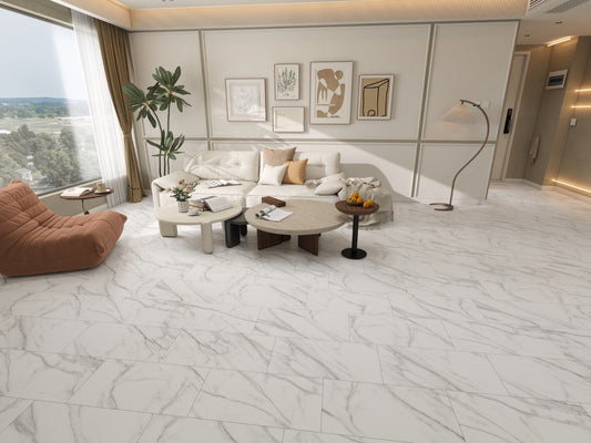 A modern living room with a large white marble-look floor tile, featuring a cream sectional sofa, a brown accent chair, and minimalist coffee tables.