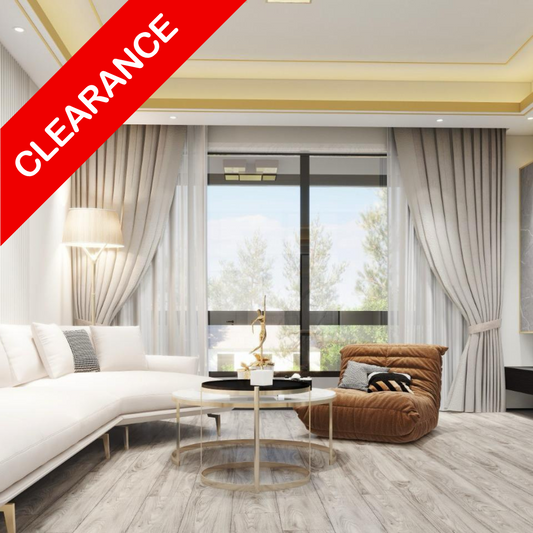 A modern living room interior showing light gray wood-look flooring, a white sectional sofa, a brown accent chair, and large windows with sheer curtains. A red diagonal banner in the top-left corner reads 'CLEARANCE'.