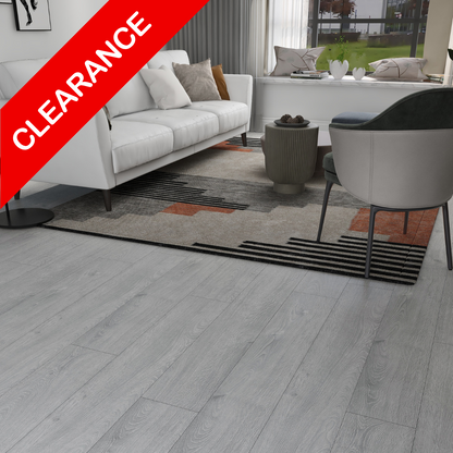 Light gray wood-look plank flooring shown in a modern living room setting with a white sofa, gray rug, and gray armchair. A red diagonal banner in the top-left corner reads 'CLEARANCE'.