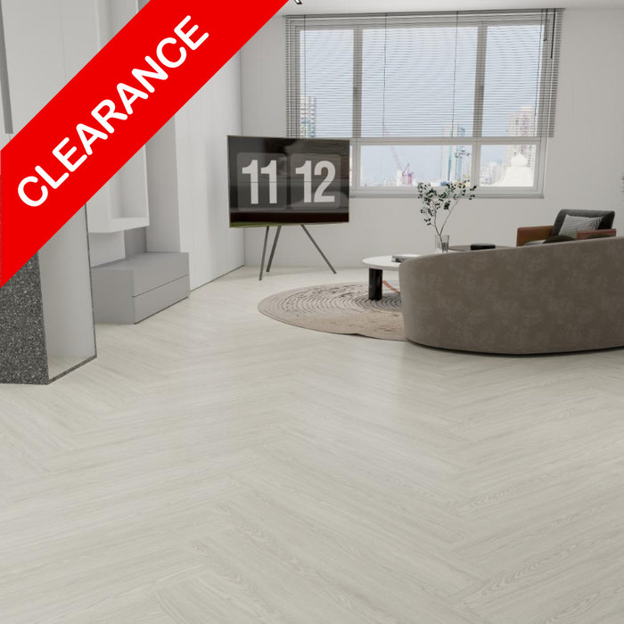 Light gray herringbone wood-look flooring shown in a modern living room setting with a curved sofa, TV, and large windows. A red diagonal banner in the top left corner reads 'CLEARANCE'.