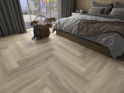 Bedroom with wooden lvt glue down light brown herringbone flooring,  bed, and basket.