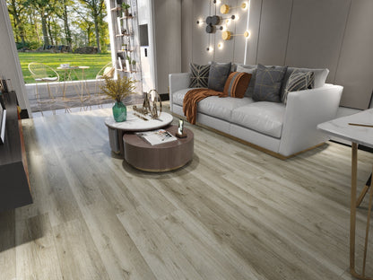 Light oak wood plank flooring shown in a modern, stylishly decorated living room with a white sofa, round coffee tables, and a large window overlooking a green garden.